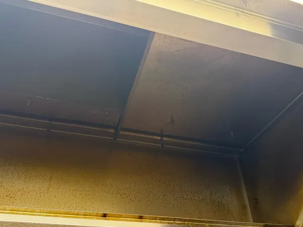 Interno di una cappa professionale prima della pulizia, con depositi di grasso giallo dietro i filtri